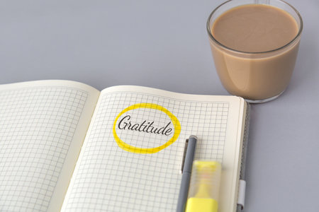 Open notebook with the handwritten word Gratitude circled in yellow, next to pen, highlighter, cup of coffee on a gray surface, symbolizing mindfulness, positivity, and emotional well-being conceptの写真素材