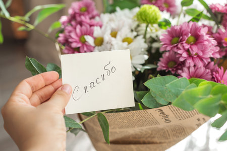 hand holds small note with text thank you on Russian written on it, above a bouquet of pink white chrysanthemums wrapped in vintage newspaper. gratitude, kindness, and a warm gesture of appreciation.の写真素材