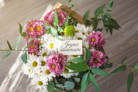 Beautiful bouquet of white pink daisies with green leaves greeting card text Joyeux anniversaire - happy birthday in French, symbolizing celebration, love, birthday wishesの写真素材