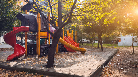 Colorful playground with slides surrounded by autumn trees and warm sunlight creating a peaceful outdoor atmosphere.の写真素材