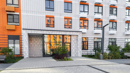 Entrance of modern residential building with geometric tiled facade in white and orange tones, large...