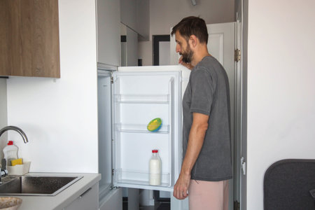 man standing in a modern kitchen looking into an open refrigerator. Concept of grocery shopping, meal planning, and domestic lifestyle.の写真素材