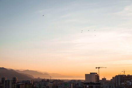 Sunset view over Batumi with silhouettes of mountains and the Black Sea in the distance. Warm evening light, soft sky colors, city skyline, cranes and buildings, peaceful landscape overlooking Gonio.の写真素材