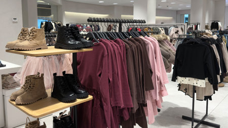 Clothing store interior with kidswear and footwear on display racks. Warm sweaters, boots and...