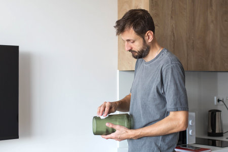 Man cleaning a glass vase in a modern kitchen, wiping dust with a cloth. Concept of household chores, home maintenance, cleanliness, daily routine and responsible lifestyle in a bright contemporary interior.の写真素材