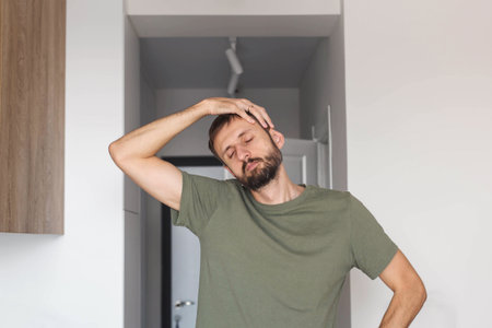 Young man stretching his neck during morning exercise at home, eyes closed and relaxed, practicing healthy routine, body mobility, wellness habits, recovery, self care and active lifestyle indoorsの写真素材