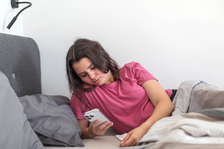 A woman lying in bed immediately checking her phone, showing signs of dopamine-driven scrolling and social media dependence early in the morning.の写真素材