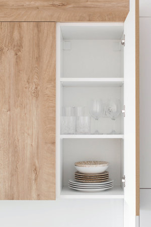 Modern kitchen cupboard with open door showing neatly arranged plates bowls and glasses white shelves and wooden facade home interior conceptの写真素材