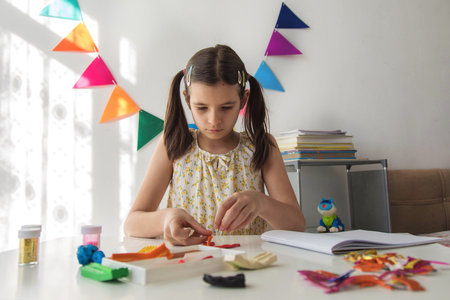 Girl creating shapes from colorful clay at home table, focused child developing creativity and fine...