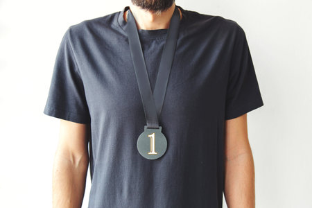 Winner concept with unrecognizable man wearing black t shirt and first place medal on ribbon against...