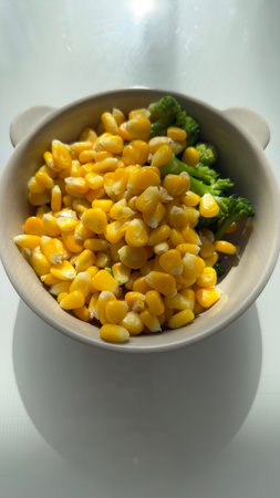 Bowl with boiled corn and broccoli on white background in sunlight, healthy vegetarian meal, concept...