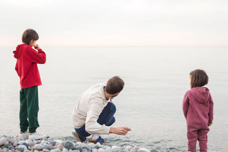 Family spending time together on a rocky beach, father and children standing at the shore and...
