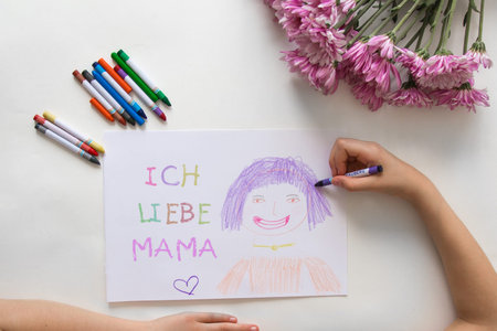 Child hand drawing colorful portrait writing ich liebe mama - i love mom in german on paper with...