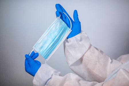 COVID-19. Facial masks on the pile. Epidemic background. Close-up. A medical worker in a protective anti-plague suit holds a maditsin mask with rubber disposable glovesの写真素材