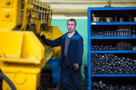 Summer, 2016 - Ussuriysk, Primorsky Krai - Ussuriysky Locomotive Repair Plant. An elderly worker in a work robe stands on the background of the machine and looks at the cameraのeditorial素材