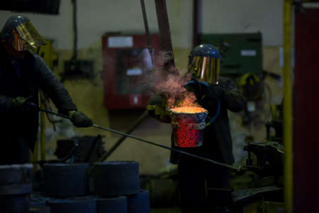 Worker man pours molten metal into molds at a steel mill