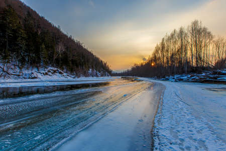 Northern landscape of Primorsky Territory, Samarga River. Frozen river in the taiga against the background of hills with coniferous trees at sunsetの写真素材