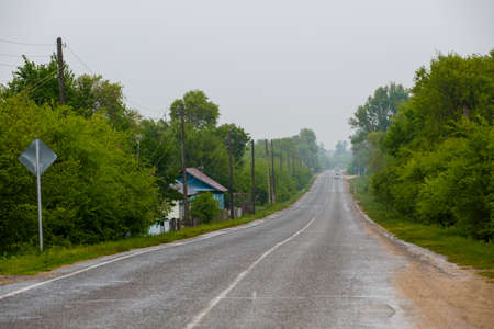 An asphalt road passes by a village with wooden housesの写真素材