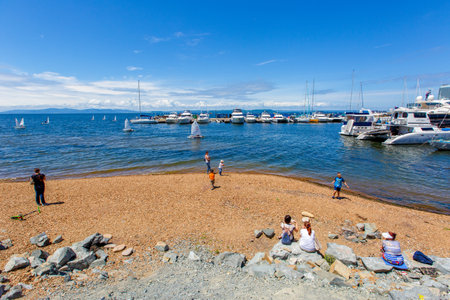 People stroll along the galician beach against the backdrop of a yacht club with beautiful boats and sailboats.のeditorial素材