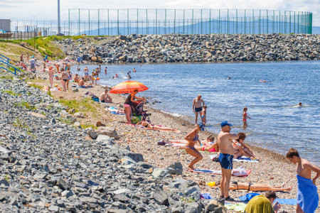 Summer, 2016 - Vladivostok, Russia - Water area of Fedorov Bay in Vladivostok. People swim and sunbathe on a public city beach in the city center against the backdrop of beautiful residential buildings and the blue seaのeditorial素材