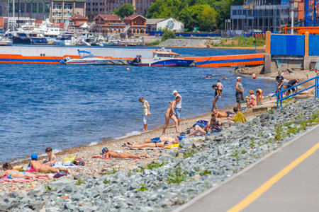 Summer, 2016 - Vladivostok, Russia - Water area of Fedorov Bay in Vladivostok. People swim and sunbathe on a public city beach in the city center against the backdrop of beautiful residential buildings and the blue seaのeditorial素材