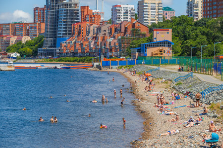 Summer, 2016 - Vladivostok, Russia - Water area of Fedorov Bay in Vladivostok. People swim and sunbathe on a public city beach in the city center against the backdrop of beautiful residential buildings and the blue seaのeditorial素材