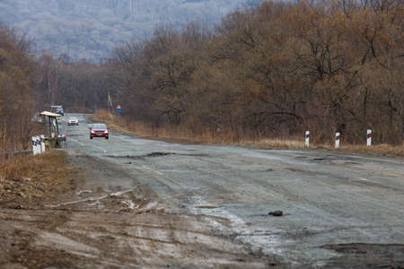 Primorsky Krai, Russia - 2016, autumn - A car drives along a bad, dead road among tall trees. Russian roads. Bad asphaltのeditorial素材