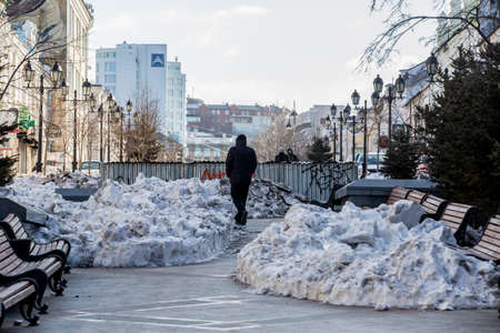 Vladivostok, Russia, 2017 - Dirty street in Vladivostok. A man walks among uncleaned snowdrifts along a pedestrian streetのeditorial素材