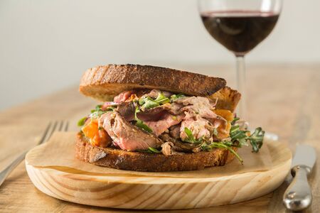 Pastrami sandwich on a wooden plate with a glass of wineの写真素材