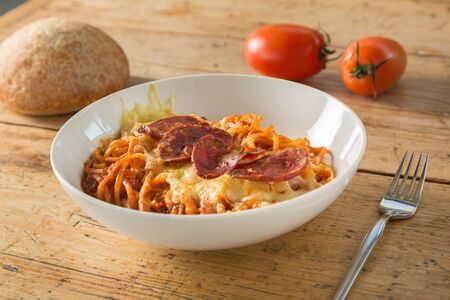 Spaghetti with tomato, with cheese on top and pepperoni, in a bowl on a wooden tableの写真素材