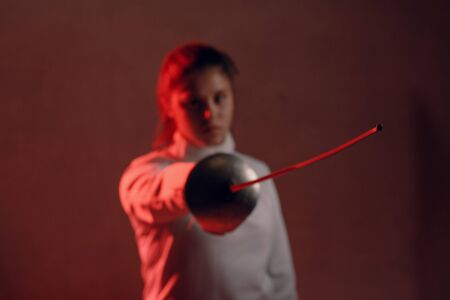 Fencer woman portrait with fencing sword in red light.の写真素材