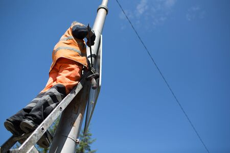 Installation road sign on pole. Road worker sets sign on blue sky background.の写真素材