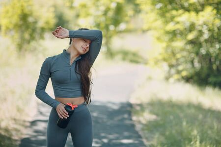 Tired runner woman jogger relaxing with bottled water after jogging in park outdoor.の写真素材