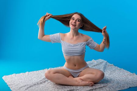 Young woman with funny emotions in white striped swimsuit lingerie isolated on blue backgroundの写真素材