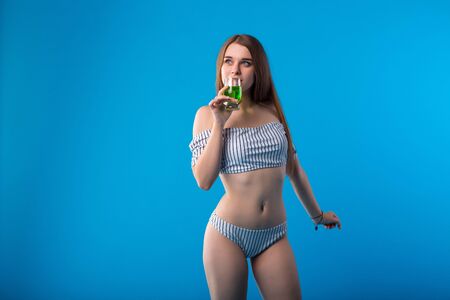 Young woman with funny emotions in white striped swimsuit lingerie isolated on blue backgroundの写真素材