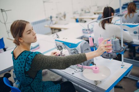 Young beautiful seamstress sews on sewing machine in factoryの写真素材