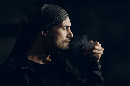 Man smoking a pipe on dark background. Back lit profile portrait.の写真素材