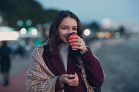 Young beautiful woman in coat and scarf with coffee cup outdoor.の写真素材
