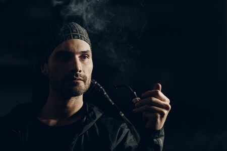 Man smoking a pipe on dark background. Back lit profile portrait.の写真素材