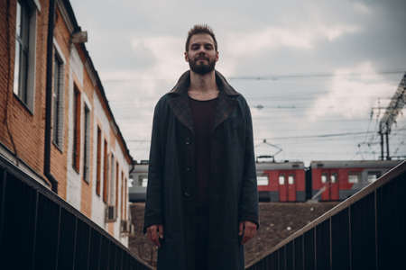 Man with beard in cloak staying on bridge against train