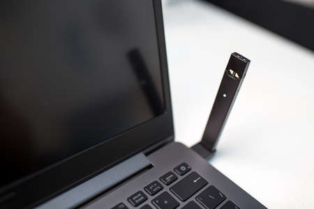 MOSCOW - 26 June 2020: Juul e-cigarette nicotine vapor stick and laptop with usb charger.のeditorial素材