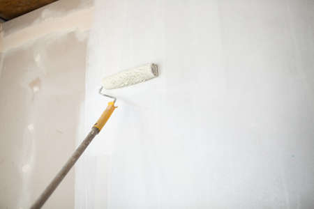White paint roller in hand with drywall wall.の写真素材
