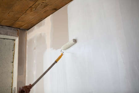White paint roller in hand with drywall wallの写真素材