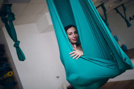 Aerial antigravity yoga concept. Woman practicing fly yoga in anti-gravity yoga studio using green hammock.の写真素材