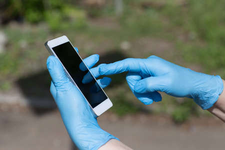Man holds mobile phone in hands in medical glovesの写真素材
