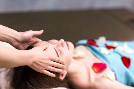 Young beautiful woman receiving head face massage in beauty spa with rose flower petals.の写真素材