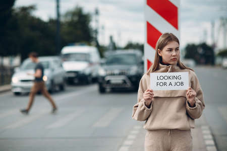 Young woman hold white paper poster in hand. Girl with white blank template sheet with inscription Looking for a job.の写真素材