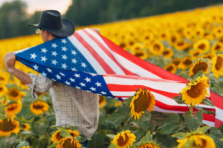 A man is walking into the sunflower field with american flag. 4th July Independence Day concept.の写真素材