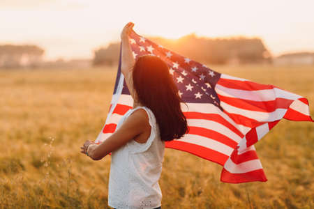 Woman farmer in the agricultural field with american flag on sunsetの写真素材