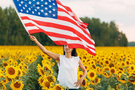 Young woman with American flag in the sunflower field. 4th of July Independence Day USA concept.の写真素材